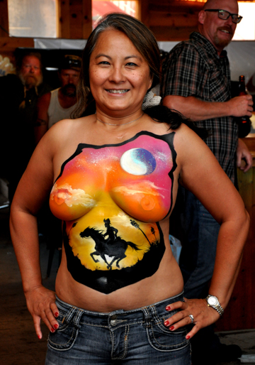 black haired woman with a painting on her chest of a pony express rider under a colorful sky and moon